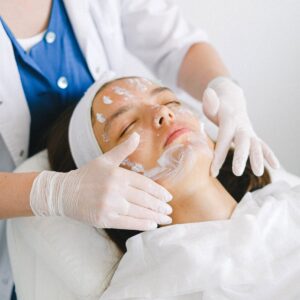 From above of crop faceless cosmetician applying facial mask on customer face during cosmetic procedure in modern spa salon